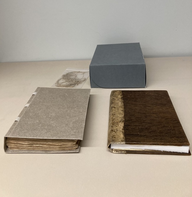 Photograph of the repaired book, with its new archival box. The old binding and threads, also shown here, have been preserved separately