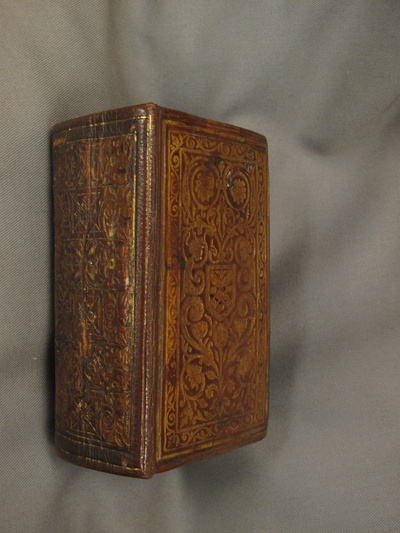 Book bound in red leather with ornate gold tooling, resting on a book-pillow