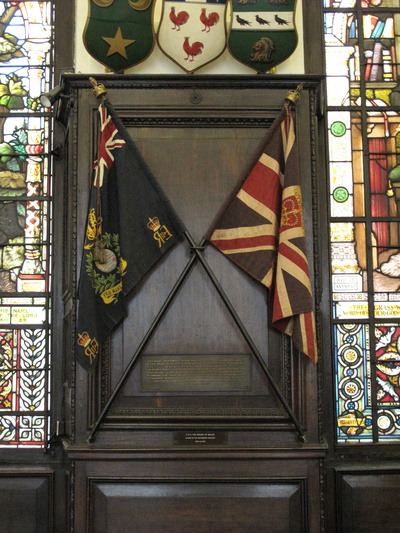 Photograph of two flags, crossed, displayed on a wooden panel in the Hall. The flags bear the colours of the Royal Marines, the Union Flag with the foul anchor and the reigning sovereign's cypher interlaced in the centre. Above is a scroll with the single battle honour Gibraltar surmounted by St Edward's Crown. Below is the globe (which represents the many battle honours the Royal Marines had earned) surrounded by a laurel wreath (which represents the Battle of Belle Isle) and below this is a scroll with the corps' motto.