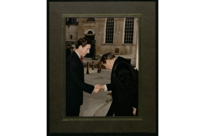 Photograph of Prince Charles on the left, shaking hands with Col. Rubens, who has his head bowed. In the background is the east wing and blue side-door of Stationers' Hall.